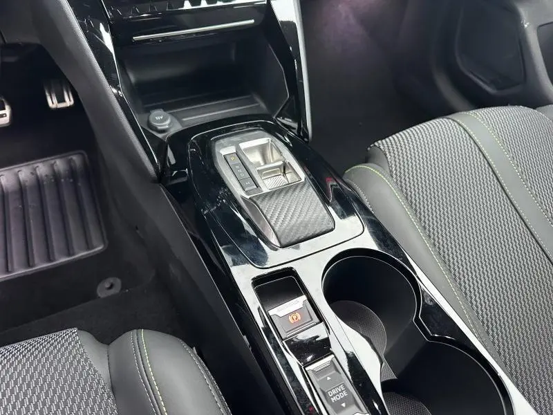 Vue rapprochée de la console centrale noire brillante avec levier de boîte auto et sièges gris à surpiqûres vertes d'une Peugeot 208 2025.