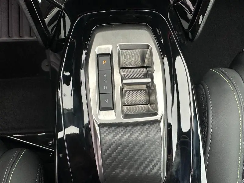 Vue rapprochée de la console centrale noire brillante du Peugeot 208 Hybrid 2025 avec commandes de boîte automatique.