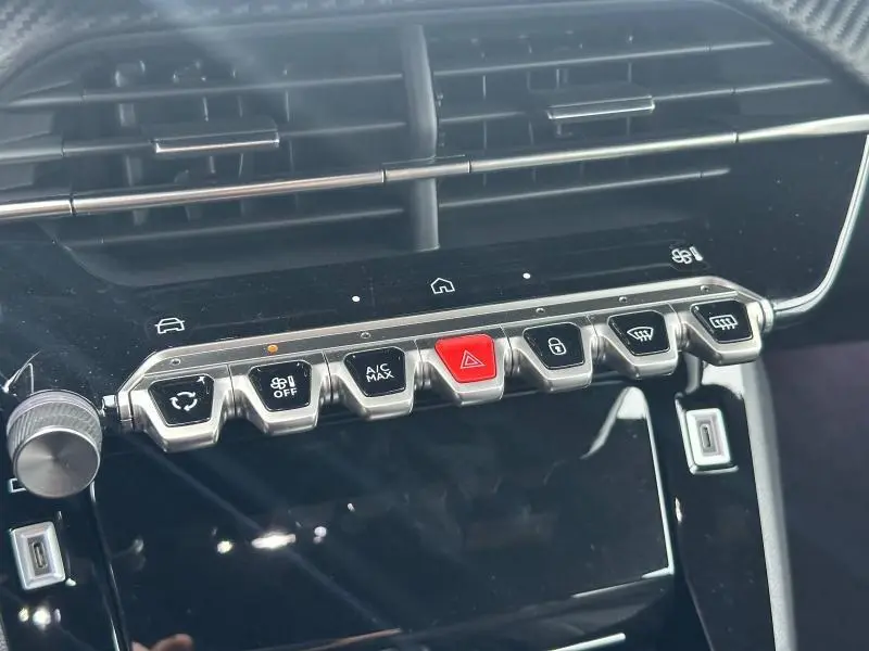 Détail de la console centrale noire du Peugeot 208 Hybrid 2025, avec rangée de boutons métalliques et rouge au centre.