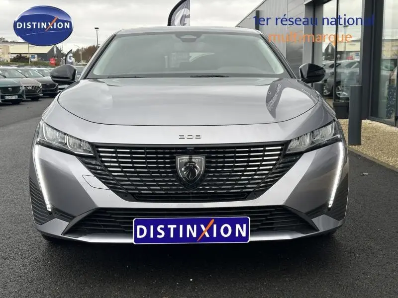 Vue frontale d'une Peugeot 308 1.2 PureTech gris Artense avec calandre noire et feux LED verticaux allumés.