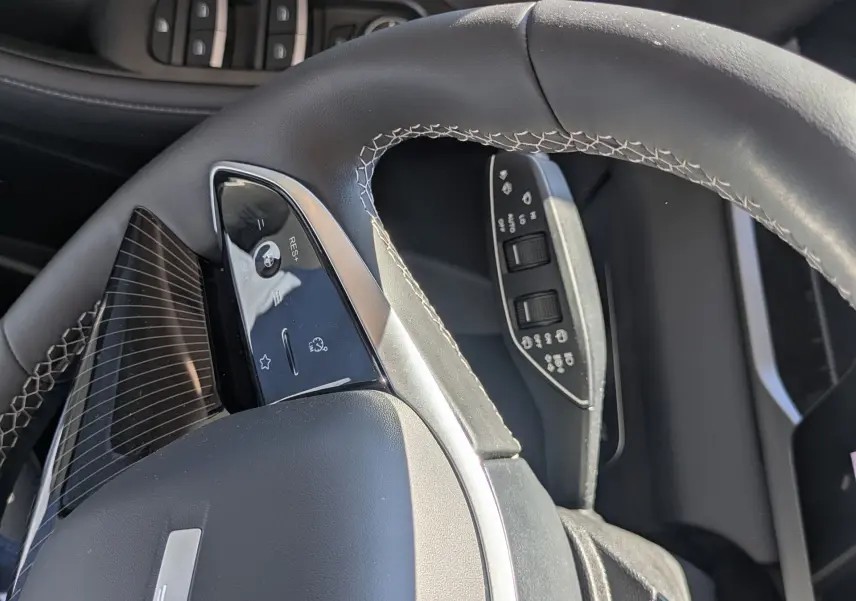 Vue rapprochée du volant cuir noir avec surpiqûres blanches et commandes intégrées du JAECOO J5, côté conducteur.