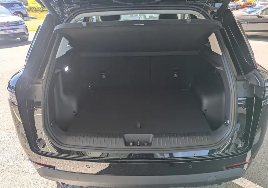 Coffre ouvert vu de l'arrière d'un JAECOO J5 noir carbone métal, montrant un espace de chargement spacieux et propre.