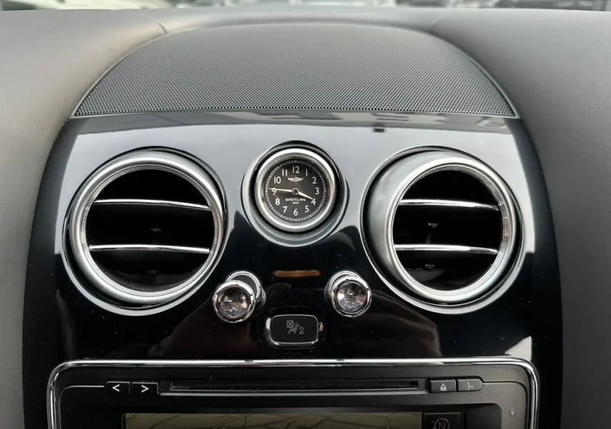 Gros plan sur l'horloge Breitling et les aérateurs ronds chromés du tableau de bord noir d'une Bentley Continental GT Mulliner 2013.