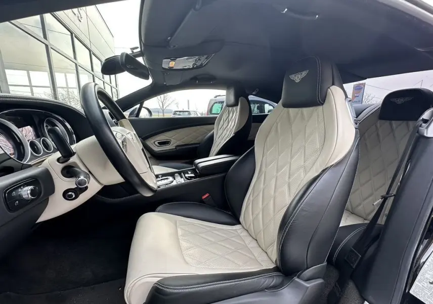 Intérieur de la Bentley Continental GT 4.0 V8 Mulliner 2013, vue côté conducteur, sièges cuir beige et noir avec logo brodé.