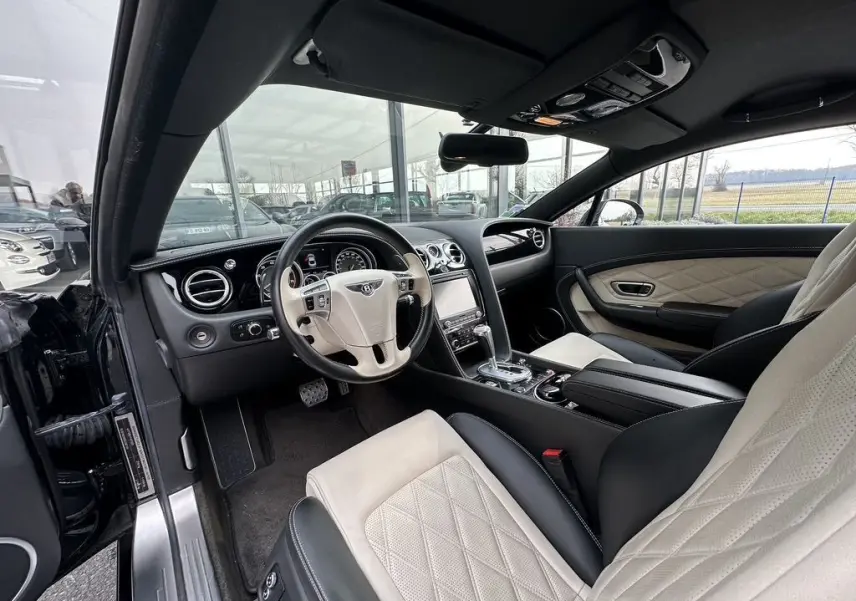 Intérieur beige et noir de la Bentley Continental GT 4.0 V8 Mulliner 2013, vue côté conducteur avec tableau de bord et volant visibles.