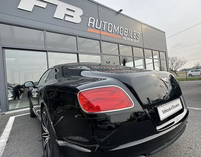 Vue 3/4 arrière droite d'une Bentley Continental GT Mulliner noire de 2013, avec feux arrière rouges et double sortie d'échappement chromée.