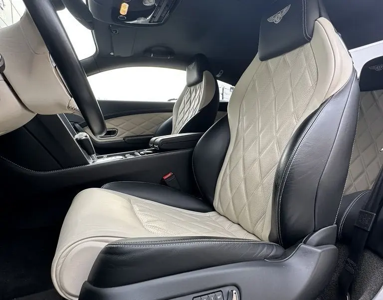 Intérieur de la Bentley Continental GT 2013 vue côté gauche, sièges cuir bicolore beige et noir avec logo Mulliner brodé.