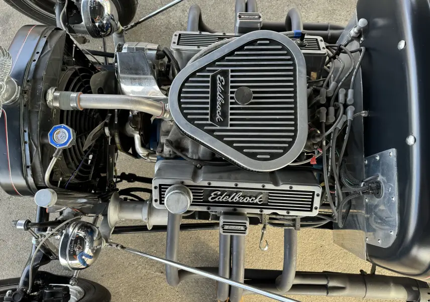 Gros plan sur le moteur V8 Edelbrock du Ford T Hot Rod noir de 1923, avec ses détails chromés et tubes d'échappement visibles.
