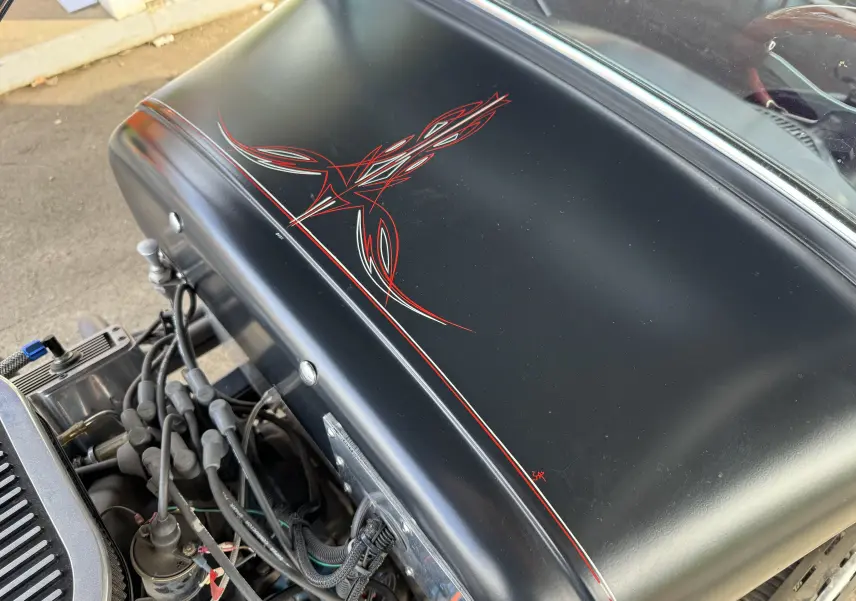 Gros plan sur le capot noir mat du Ford T Hot Rod 1923 avec motifs rouges peints à la main, moteur V8 visible dessous.