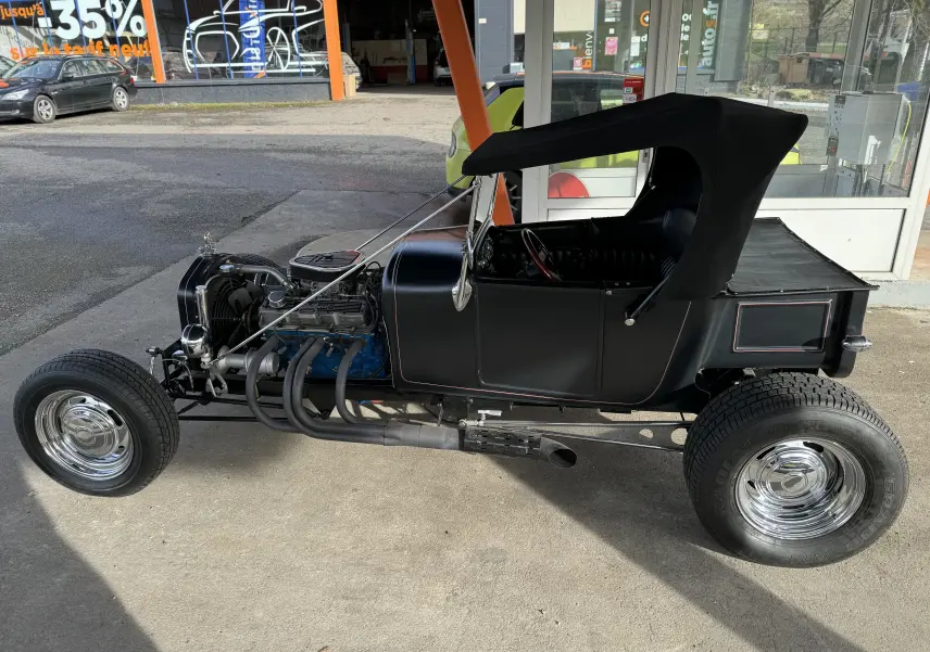 Vue de profil côté gauche d'une Ford T Hot Rod V8 noire décapotable, moteur apparent et jantes chromées.