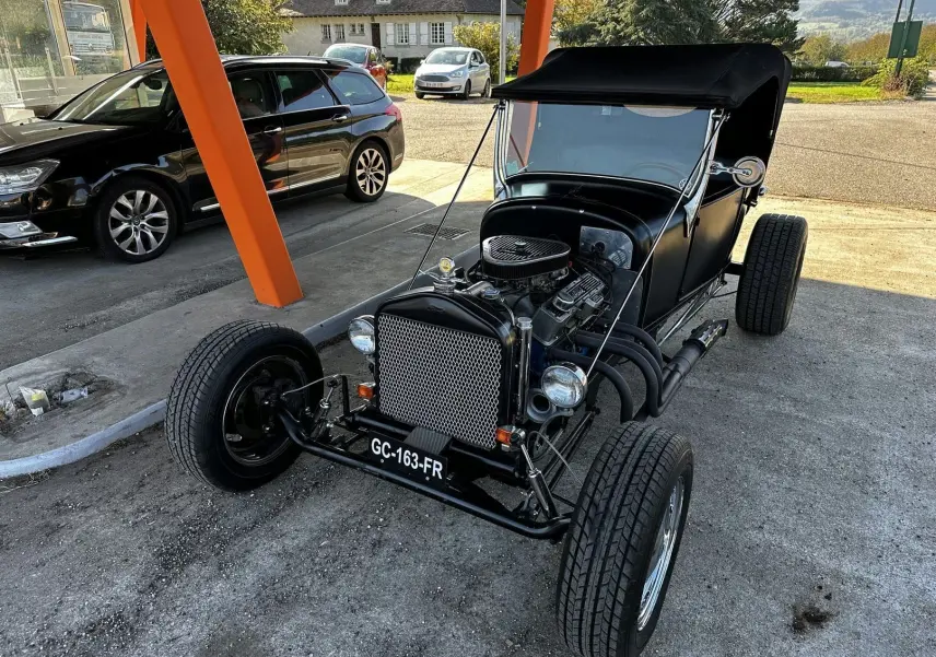 Ford T Hot Rod V8 noir vu en 3/4 avant droit, capote noire relevée et moteur V8 apparent au détail.