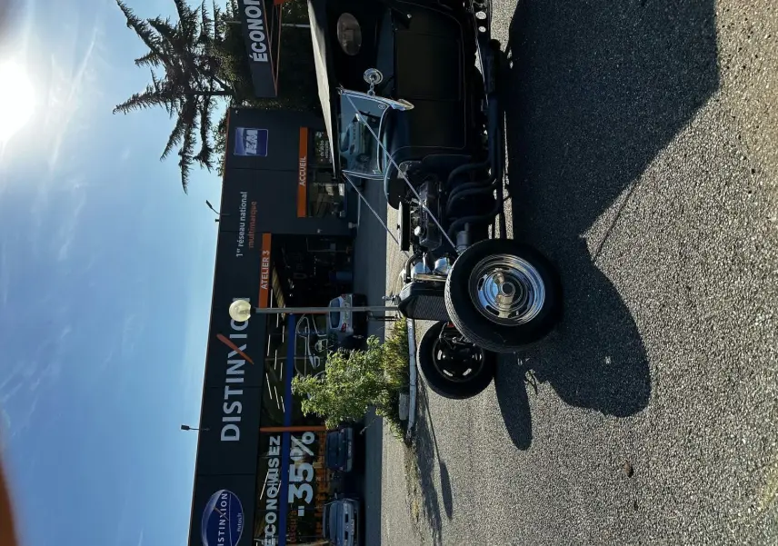 Ford T Hot Rod V8 noir vue 3/4 avant droit, capote relevée et jantes chromées brillantes sur parking.