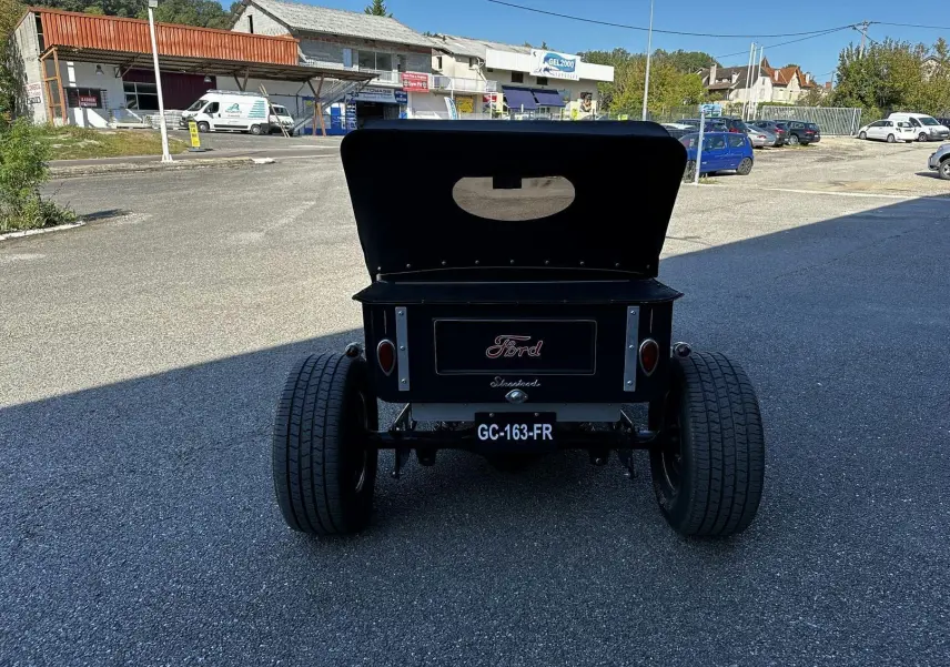 Vue arrière d'une Ford T Hot Rod V8 noire de 1923 avec capote relevée et larges pneus arrière visibles.