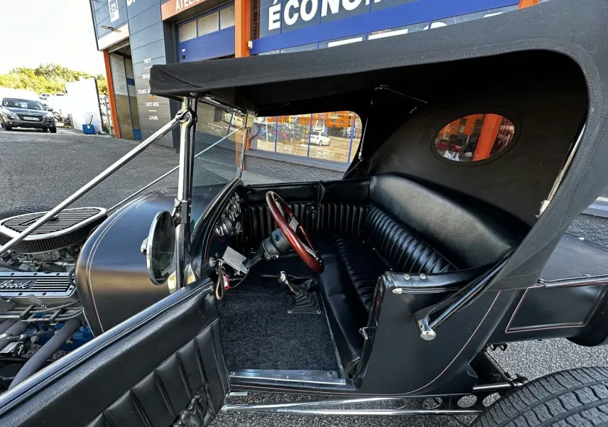 Vue côté gauche intérieur du Ford T Hot Rod V8 noir, banquette cuir et volant bois visibles sous capote décapotable.