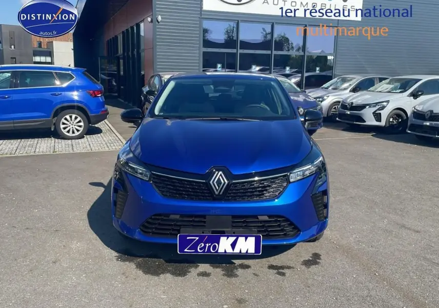 Vue frontale d'une Renault Clio V bleu iron avec calandre noire et logo Renault proéminent, stationnée en extérieur.