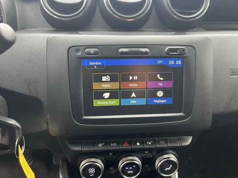 Écran tactile central du tableau de bord du Dacia Duster blanc glacier avec commandes clim et modes de conduite visibles