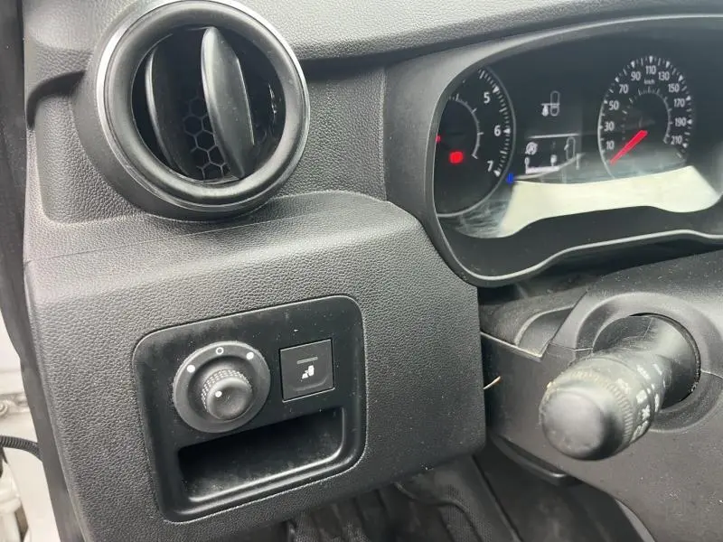 Détail du tableau de bord noir du Dacia Duster blanc, avec commandes de réglage des rétroviseurs et compteurs visibles.