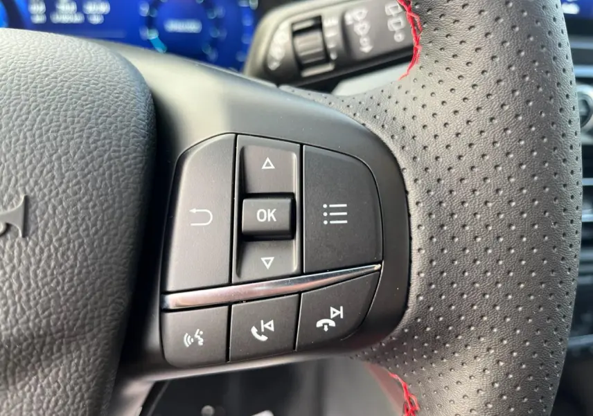 Gros plan sur les commandes au volant à gauche du Ford Kuga ST-Line 2022, cuir perforé avec surpiqûres rouges.