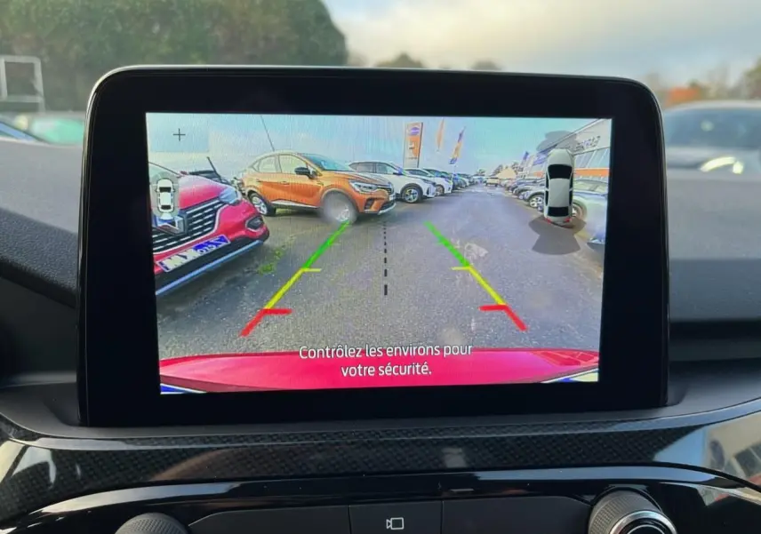 Vue écran intérieur montrant la caméra arrière du Ford Kuga rouge Lucifer en stationnement avec lignes d’aide au recul colorées.