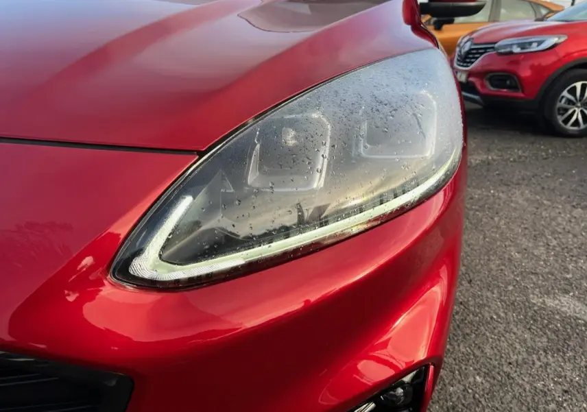 Gros plan sur le phare avant droit du Ford Kuga 1.5 EcoBoost rouge Lucifer avec peinture métallisée.