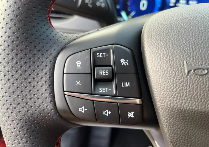 Gros plan sur les commandes au volant côté gauche du Ford Kuga rouge Lucifer, avec surpiqûres rouges visibles.