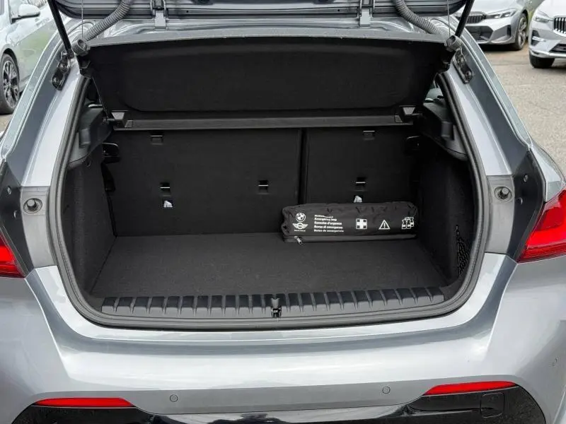 Coffre ouvert vu de l'arrière d'une BMW Série 1 118dA 2022 gris métallisé avec trousse de secours noire à l'intérieur.