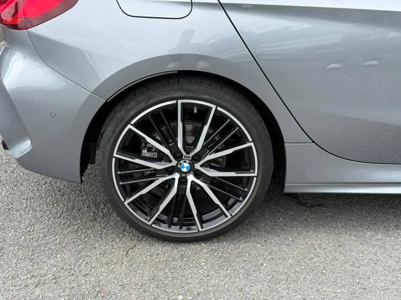 Gros plan sur la roue arrière gauche d'une BMW Série 1 118dA M Sport 2022 en Saphirschwarz métallisé avec jante alu noire et argent.