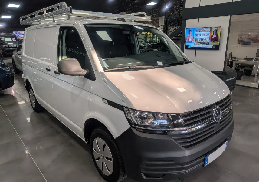 Volkswagen Transporter 6.1 blanc Candy en 3/4 avant droit avec galerie de toit en intérieur showroom.