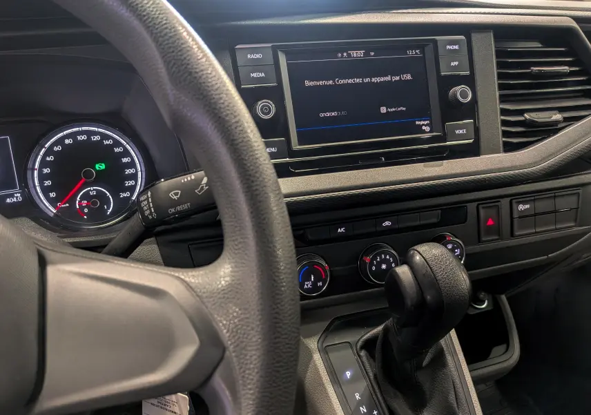 Vue intérieure du tableau de bord du Volkswagen Transporter 6.1 blanc, avec écran tactile et levier de vitesses automatique.