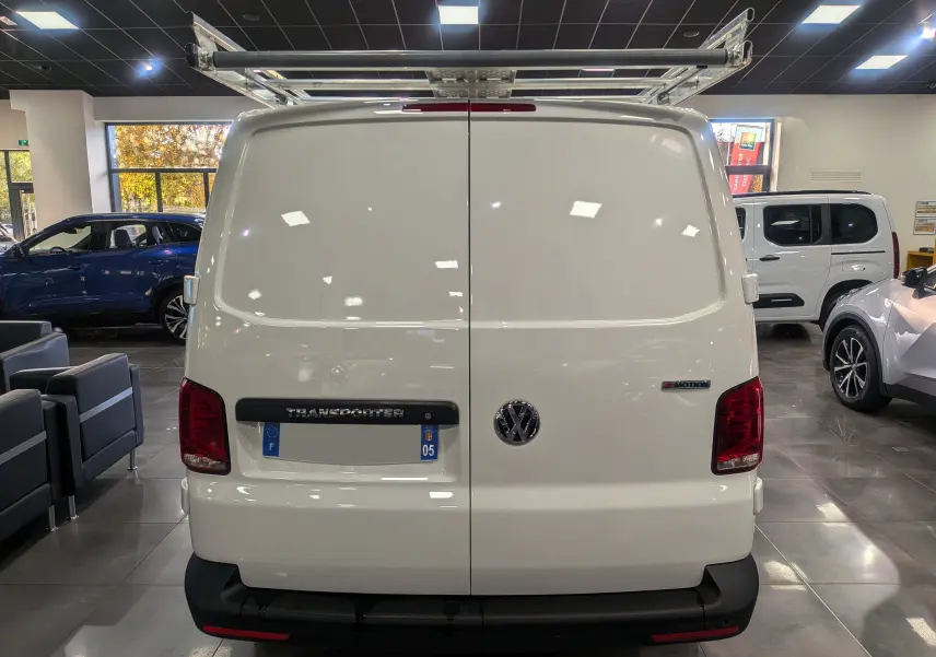 Vue arrière d'un Volkswagen Transporter 6.1 blanc Candy avec galerie de toit et badge 4MOTION visible en intérieur showroom.