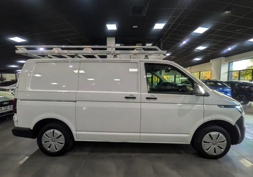 Vue de profil côté gauche du Volkswagen Transporter 6.1 blanc Candy avec galerie de toit en intérieur de showroom.
