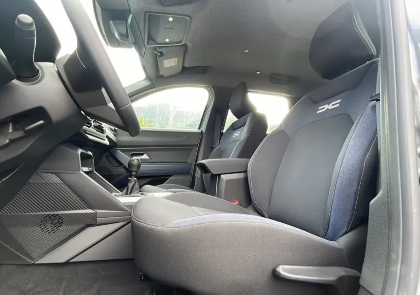 Vue intérieure côté conducteur du Dacia Bigster 2025, sièges noirs et gris avec logo DC brodé sur appuie-tête.