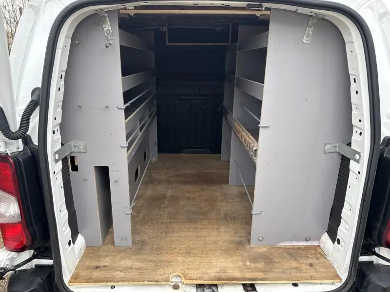 Vue arrière ouverte du Citroën Berlingo Fourgon blanc Banquise montrant l'aménagement intérieur avec étagères grises et plancher bois.
