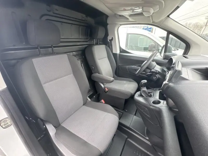 Vue intérieure côté conducteur du Citroën Berlingo Fourgon blanc, montrant les sièges tissu gris et la console centrale.