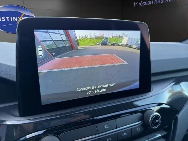 Écran intérieur du Ford Kuga 2024 montrant la caméra de recul avec vue arrière du véhicule gris en stationnement.