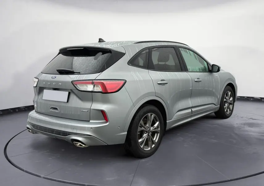 Vue 3/4 arrière droite d'un Ford Kuga gris 2024 hybride essence avec finition ST-Line X et double sortie d'échappement.