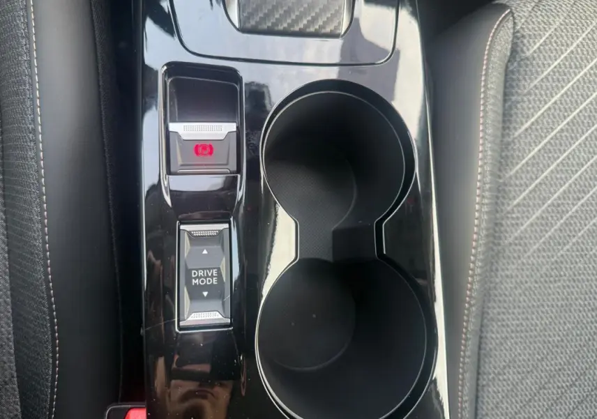 Gros plan sur la console centrale noire brillante de la Peugeot 208 gris, avec bouton frein à main électronique et mode de conduite.