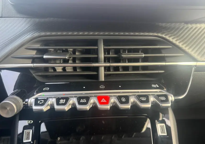 Détail du tableau de bord de la Peugeot 208 gris, montrant les commandes centrales et les aérateurs au-dessus.