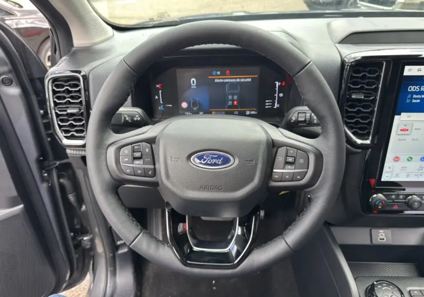 Vue intérieure centrée sur le volant cuir multifonctions du Ford Ranger gris carbone avec tableau de bord digital et écran tactile.