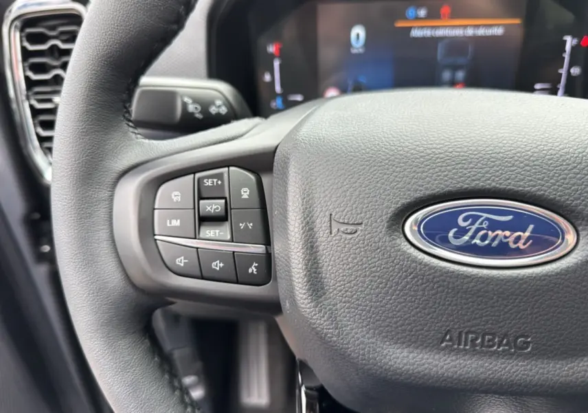 Gros plan sur le volant cuir gris du Ford Ranger 2026 avec commandes multifonctions et logo Ford central.