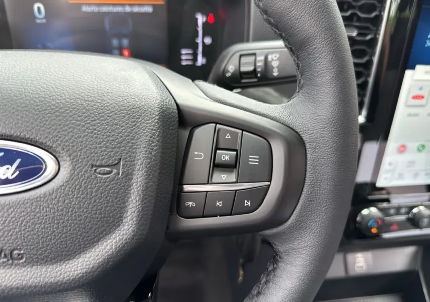 Gros plan sur le volant cuir du Ford Ranger gris carbone, avec commandes multifonctions et tableau de bord numérique en arrière-plan.
