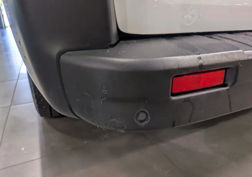 Gros plan sur le pare-chocs arrière droit noir avec un réflecteur rouge du Renault Trafic Fourgon blanc Glacier.