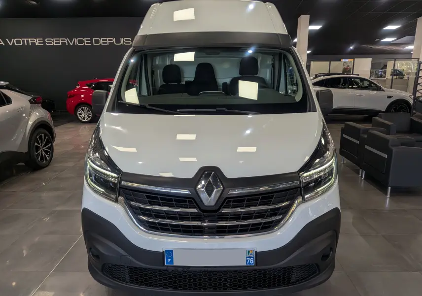 Vue frontale d'un Renault Trafic Fourgon blanc glacier L2H2 2021 en showroom, avec calandre noire et logo Renault visible.