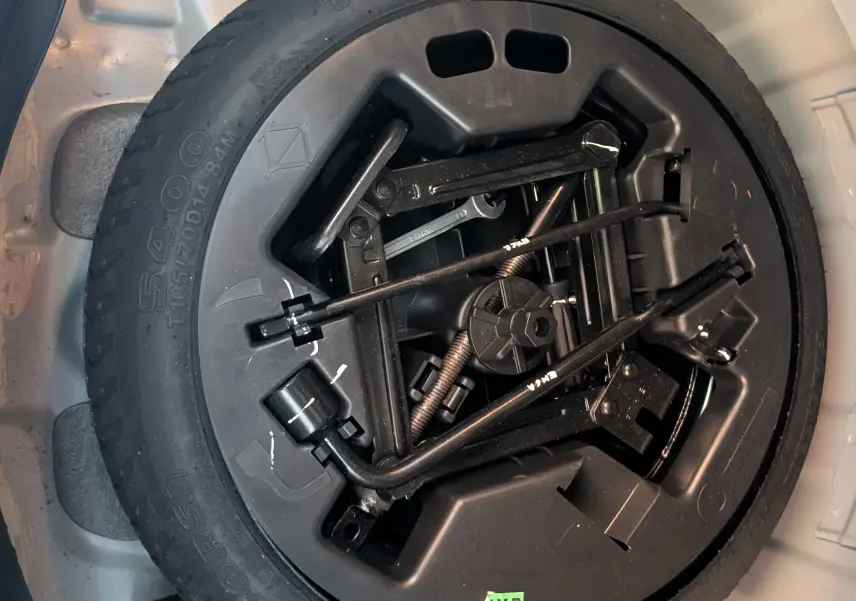 Gros plan sur la roue de secours noire et ses outils de bord dans le coffre gris clair d'une Hyundai i10 2010.