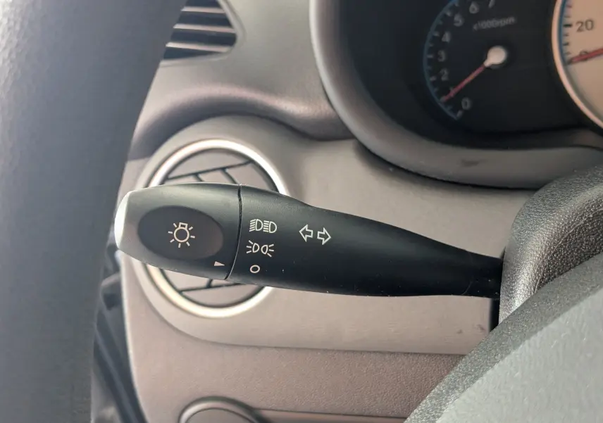 Gros plan sur la commande des clignotants et phares à gauche du volant dans l’habitacle gris d’une Hyundai i10 gris clair 2010.