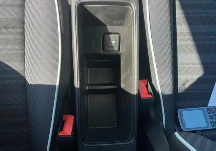 Vue plongeante sur le rangement central noir entre les sièges gris avec surpiqûres blanches de la Fiat 500 électrique blanche.