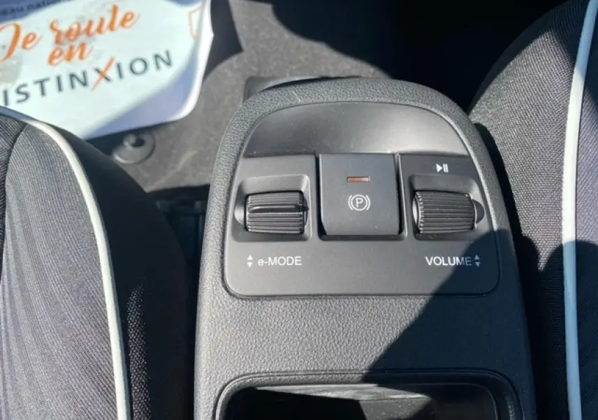 Gros plan sur la console centrale de la Fiat 500 électrique blanche, montrant les commandes e-mode, frein à main électrique et volume.