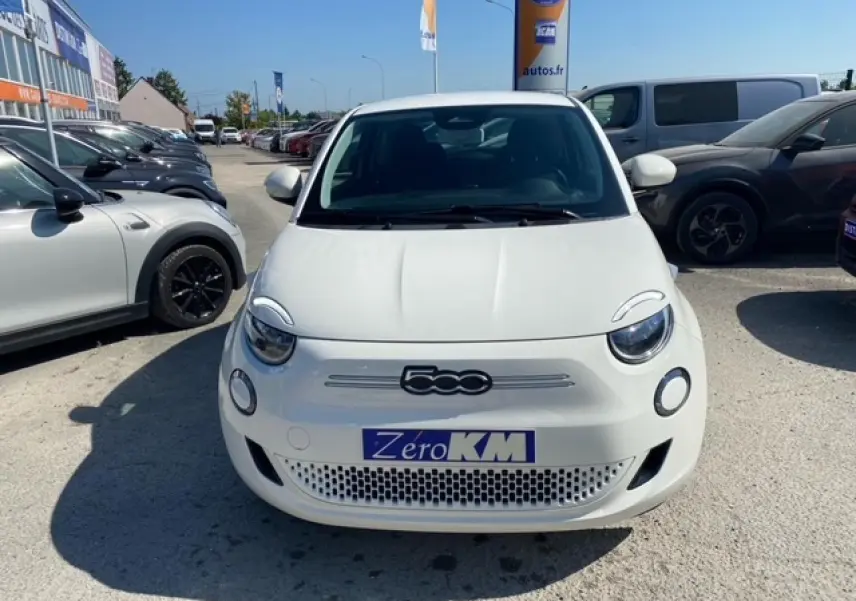 Vue de face d'une FIAT 500 électrique blanche Ice White avec logo 500 et plaque Zéro KM visible.