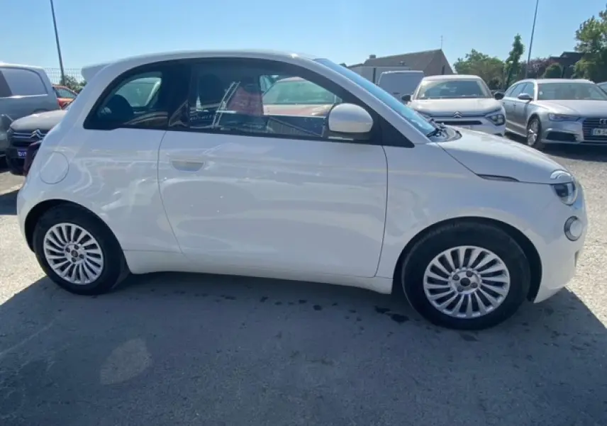 Vue de profil côté gauche d'une FIAT 500 électrique blanche métallisée, avec jantes originales et silhouette compacte.