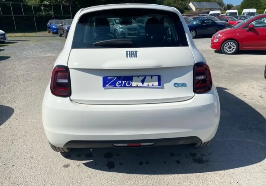 Vue arrière d'une FIAT 500 électrique blanche 2022 avec logo bleu et plaque "Zero KM" sur un parking extérieur.